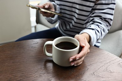 Photo of Woman with smartphone having coffee break at wooden table in cafe, closeup