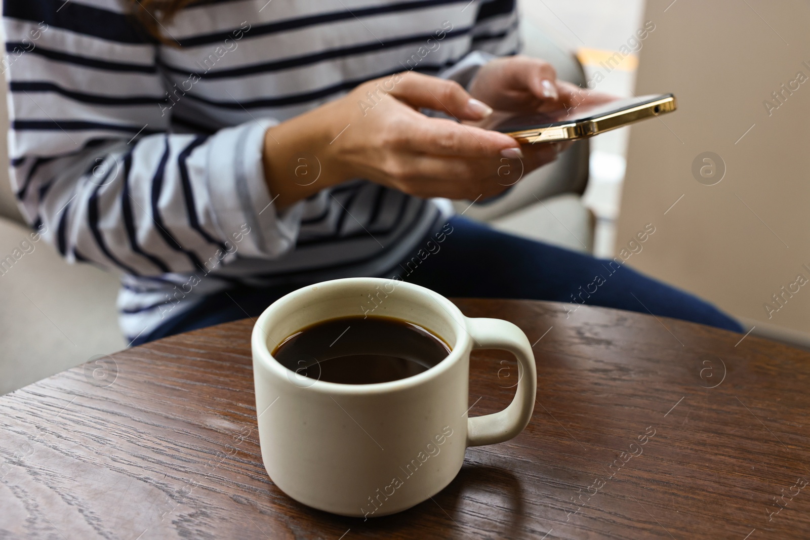 Photo of Woman with smartphone having coffee break at wooden table in cafe, closeup