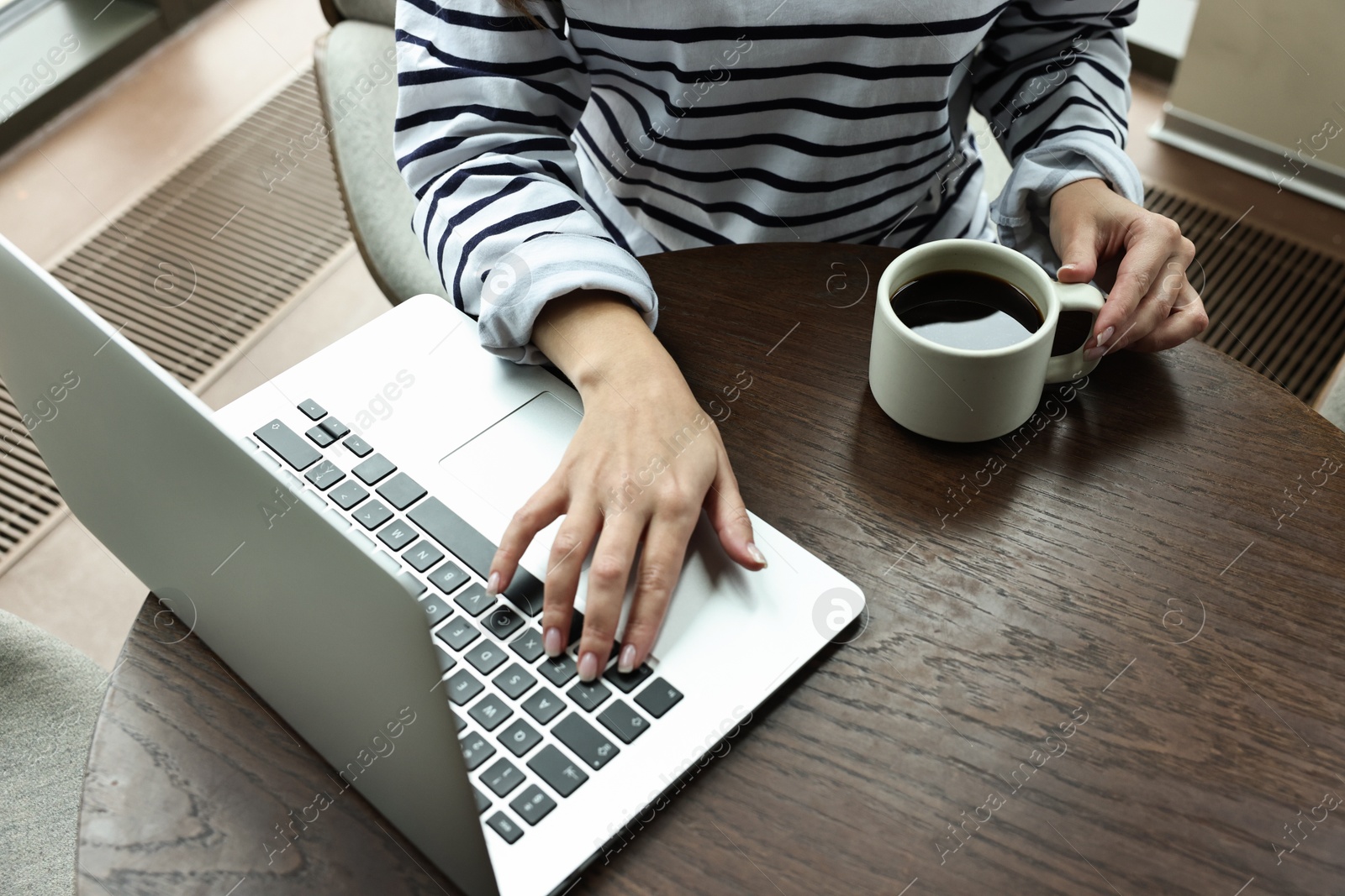 Photo of Woman with laptop having coffee break at wooden table in cafe, closeup