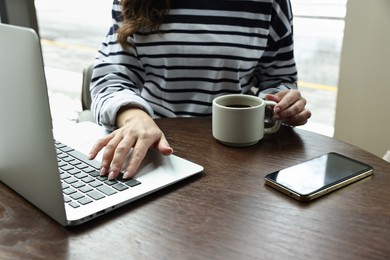 Photo of Woman with laptop and smartphone having coffee break at wooden table in cafe, closeup