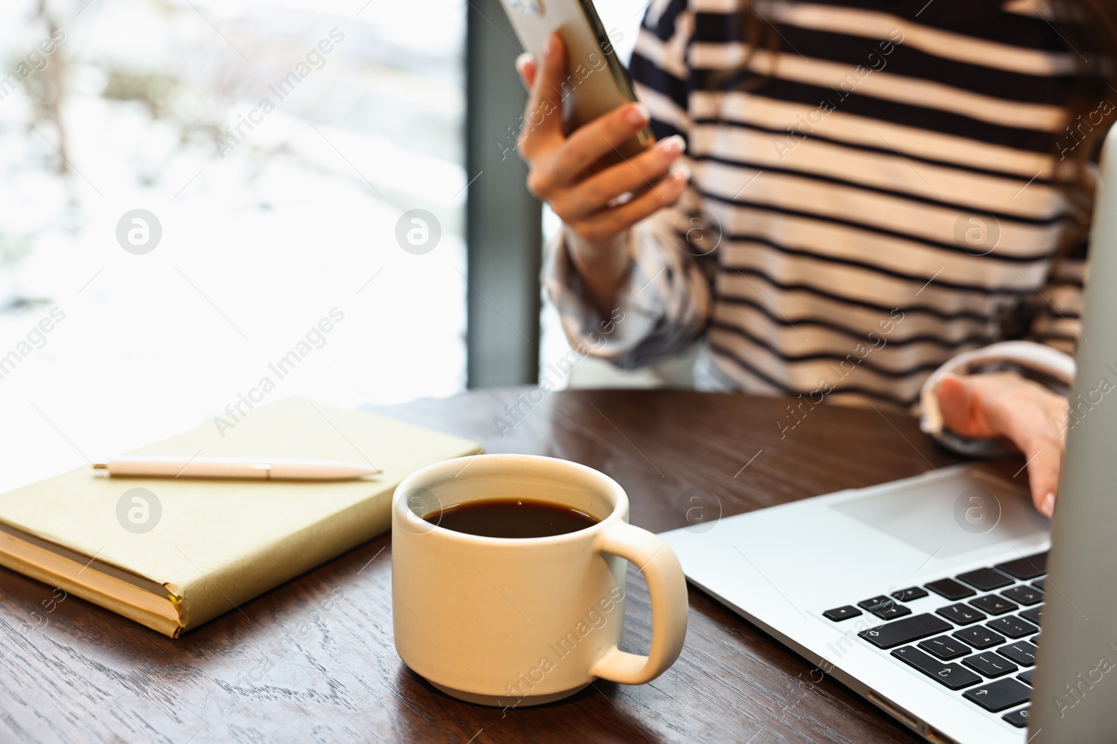 Photo of Woman with smartphone having coffee break at wooden table in cafe, closeup