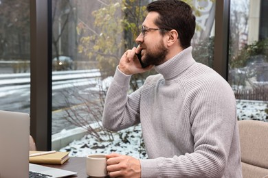 Photo of Businessman talking on smartphone during coffee break in cafe