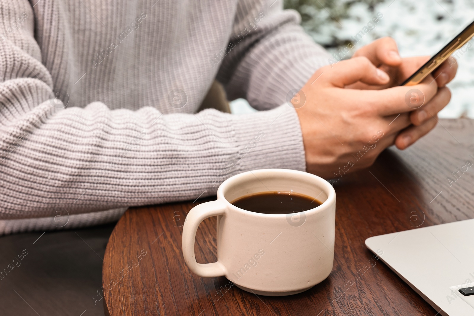 Photo of Man with smartphone having coffee break at wooden table in cafe, closeup