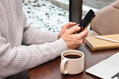 Photo of Man with smartphone having coffee break at wooden table in cafe, closeup