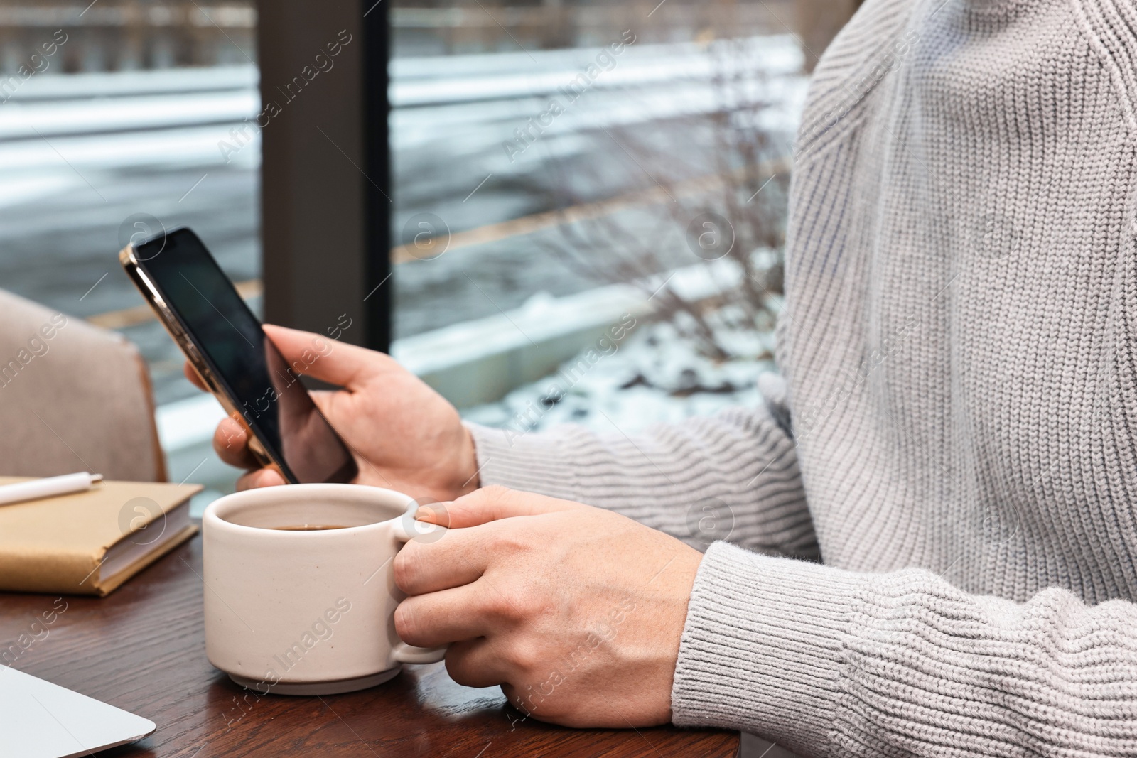 Photo of Man with smartphone having coffee break at wooden table in cafe, closeup