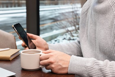 Photo of Man with smartphone having coffee break at wooden table in cafe, closeup