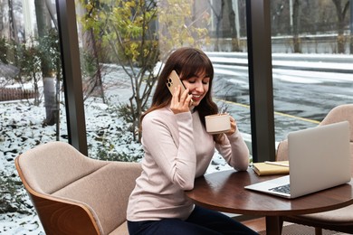 Photo of Smiling businesswoman talking by smartphone during coffee break in cafe