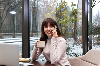 Photo of Smiling businesswoman talking by smartphone during coffee break in cafe