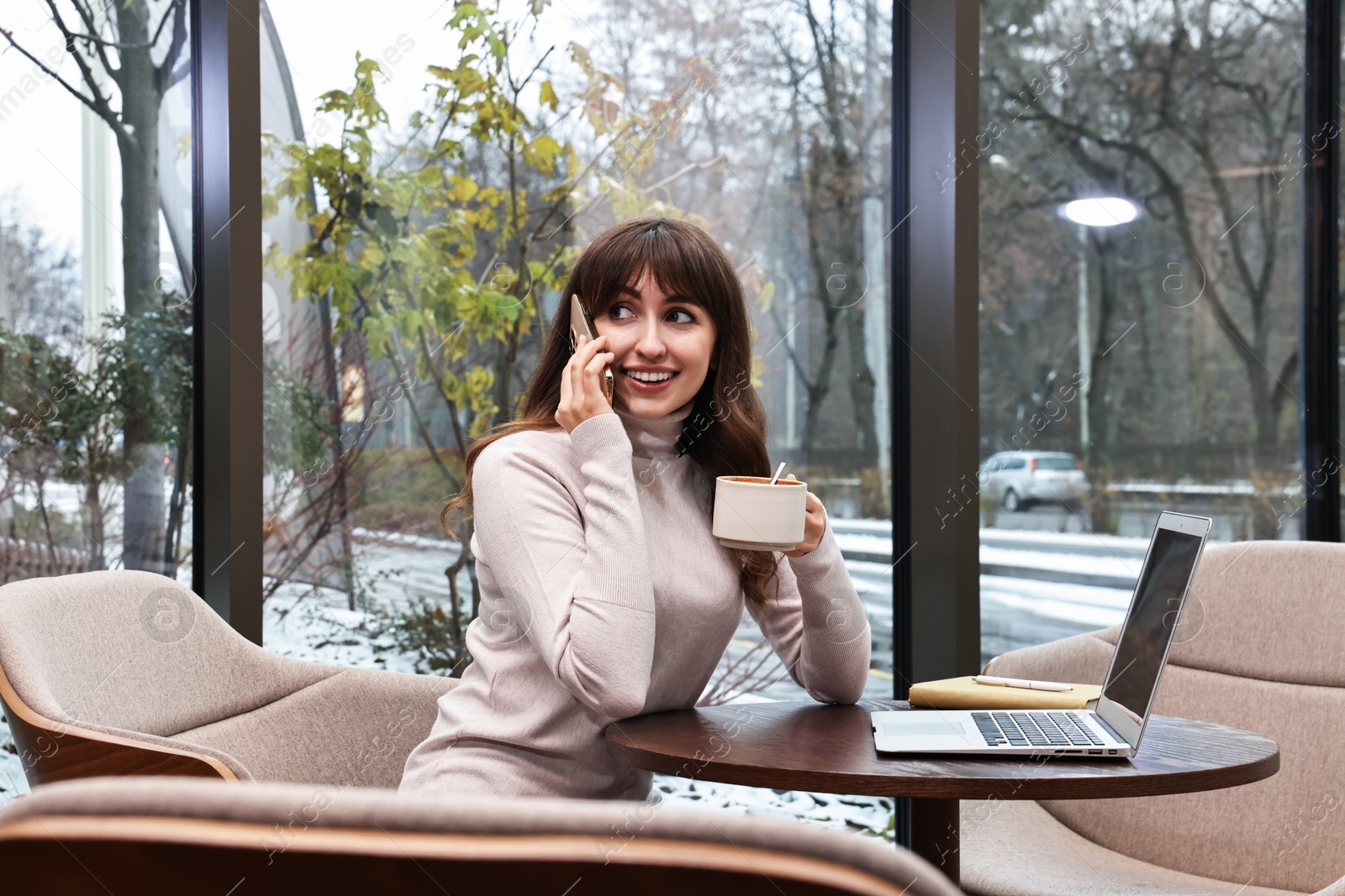 Photo of Smiling businesswoman talking by smartphone during coffee break in cafe