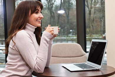 Photo of Smiling woman with laptop having coffee break at wooden table in cafe