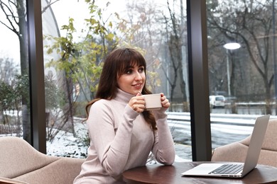 Photo of Smiling woman with laptop having coffee break at wooden table in cafe