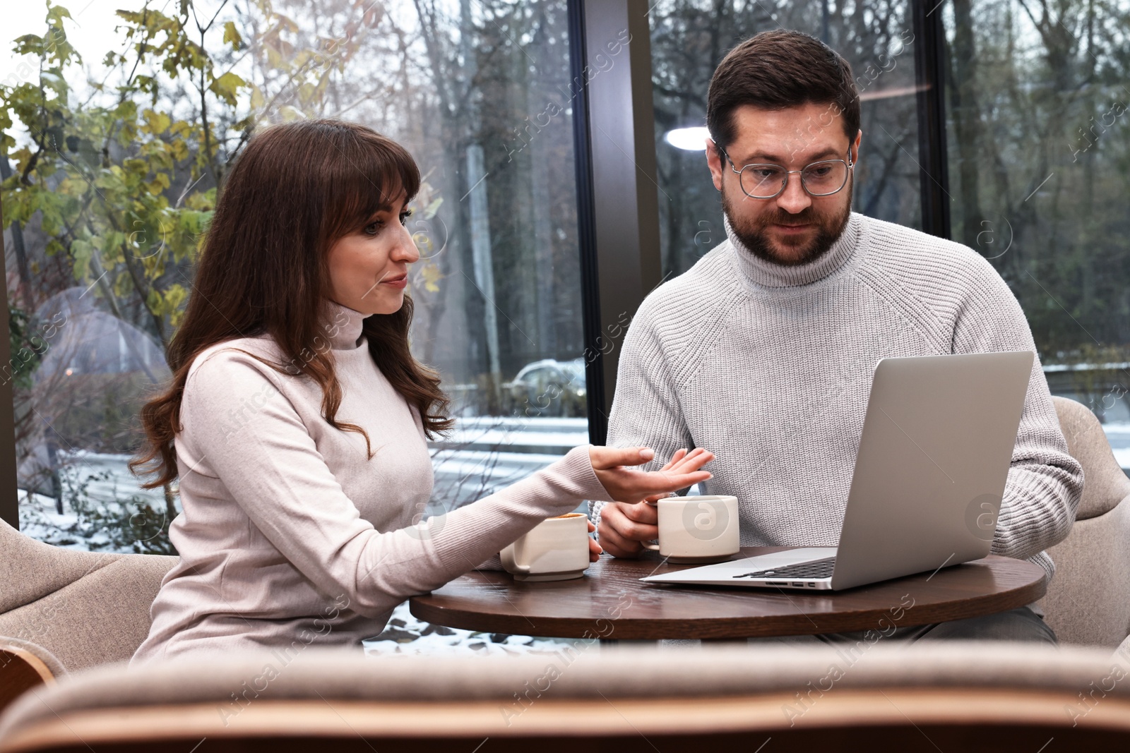 Photo of Colleagues with laptop having coffee break at wooden table in cafe