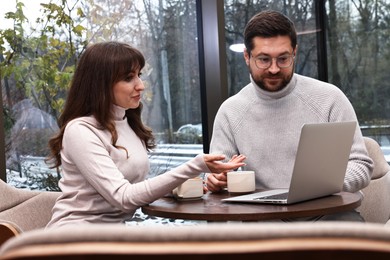 Photo of Colleagues with laptop having coffee break at wooden table in cafe