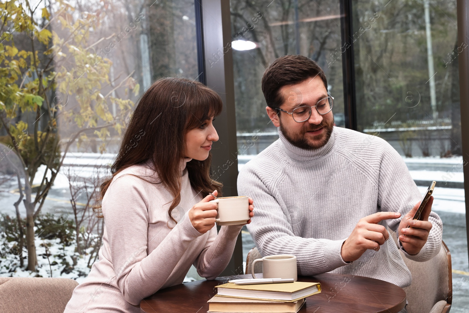 Photo of Colleagues with smartphone having coffee break at wooden table in cafe