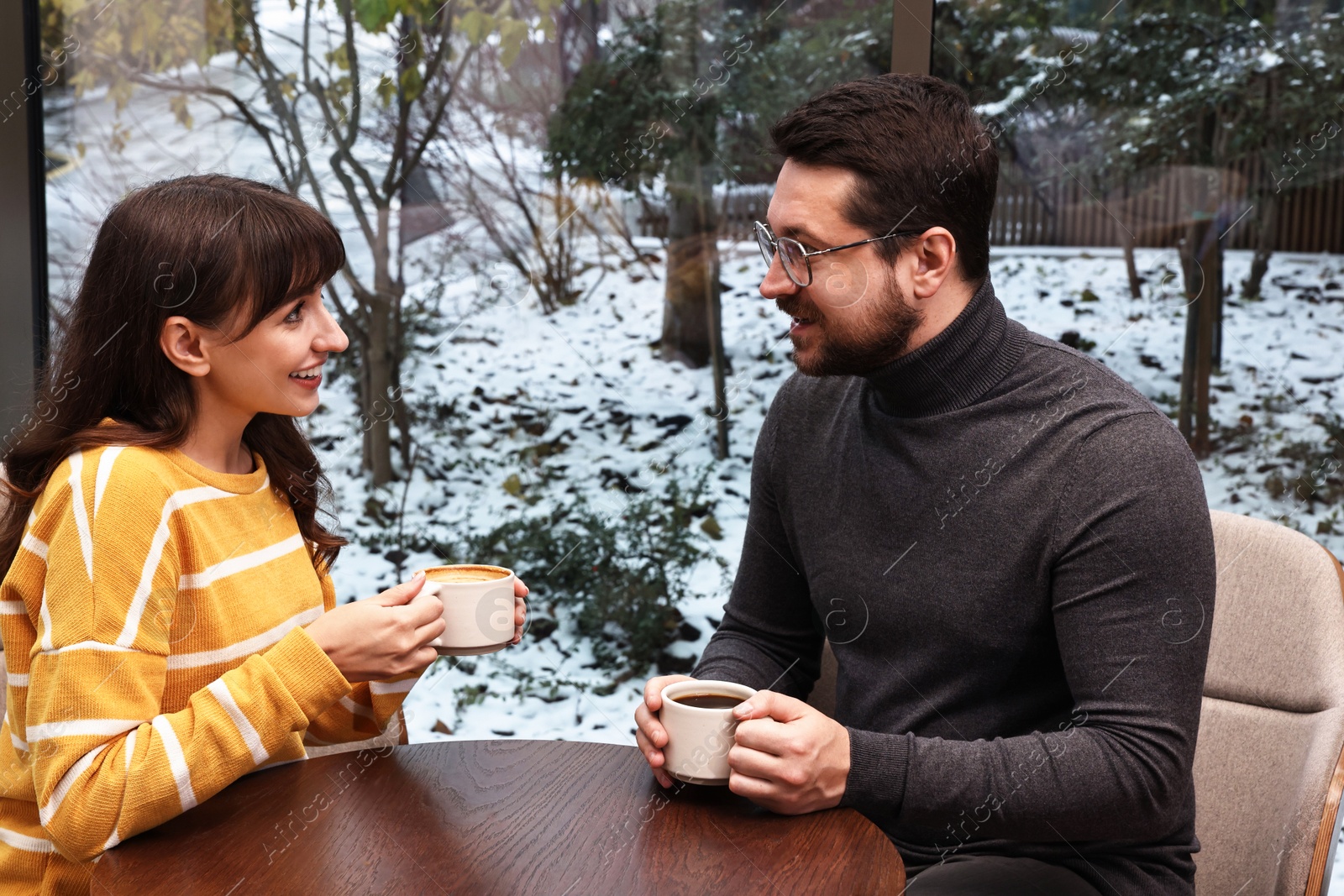 Photo of Happy colleagues talking during coffee break at wooden table in cafe