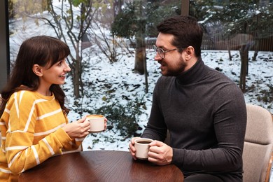 Photo of Happy colleagues talking during coffee break at wooden table in cafe