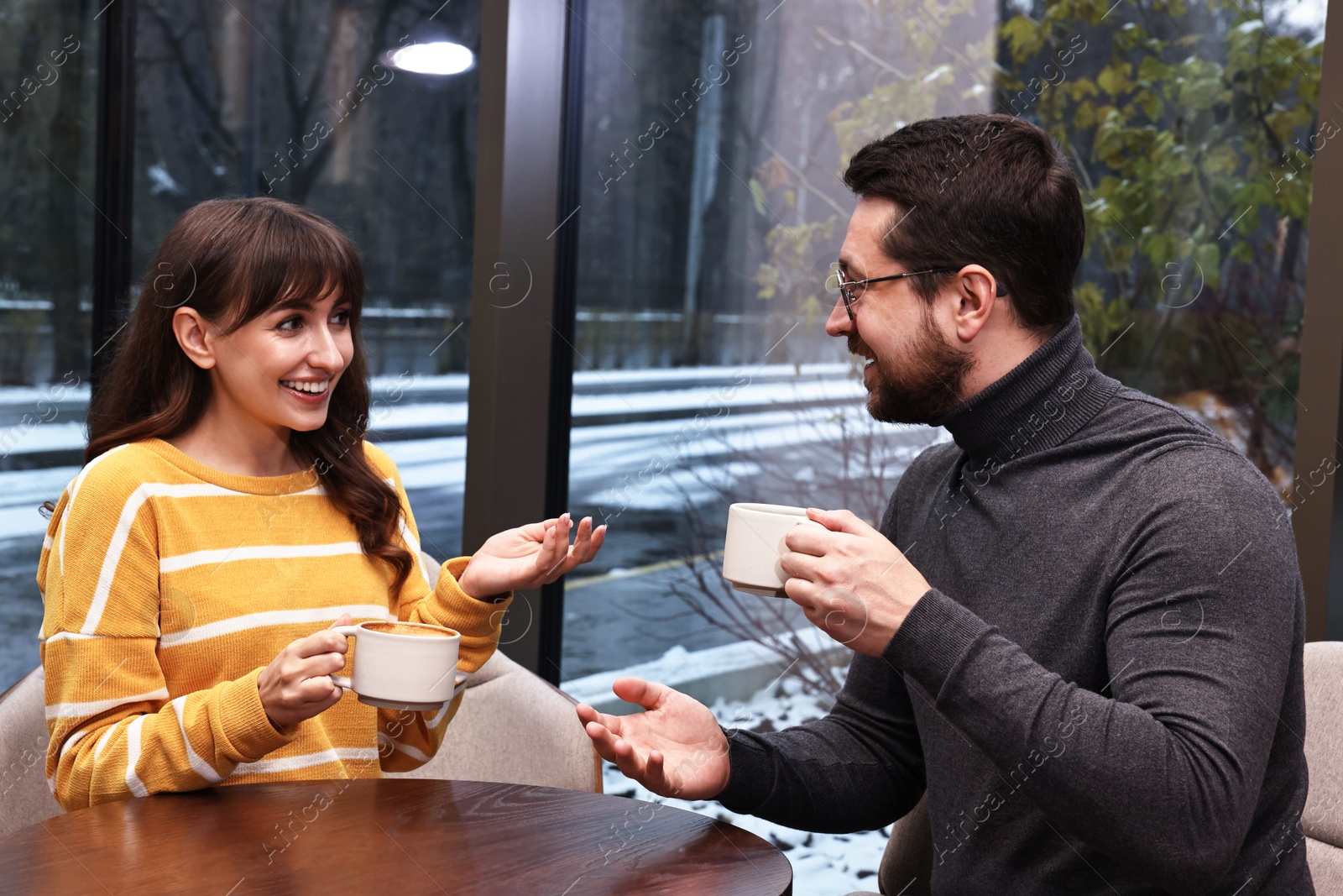 Photo of Happy colleagues talking during coffee break at wooden table in cafe