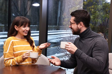 Photo of Happy colleagues talking during coffee break at wooden table in cafe