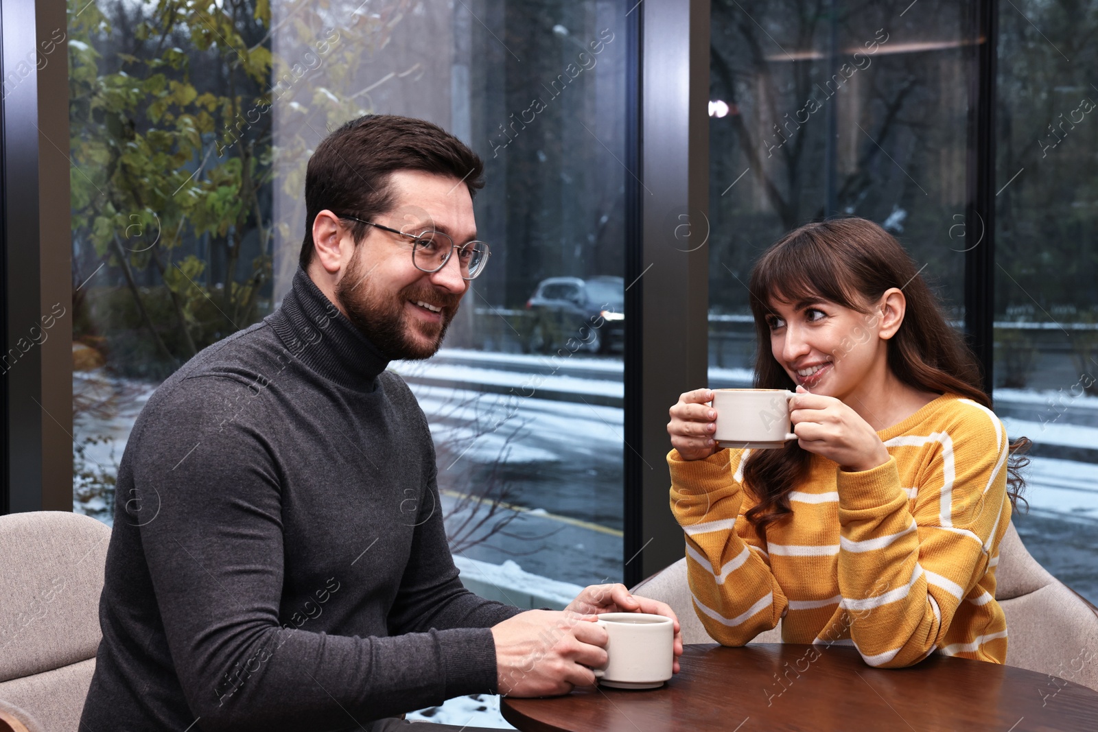 Photo of Happy colleagues talking during coffee break at wooden table in cafe