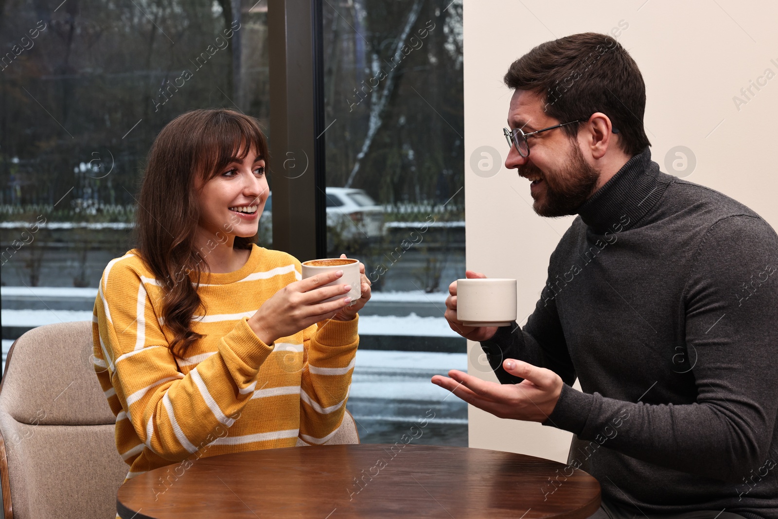 Photo of Happy colleagues talking during coffee break at wooden table in cafe