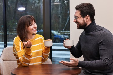 Photo of Happy colleagues talking during coffee break at wooden table in cafe