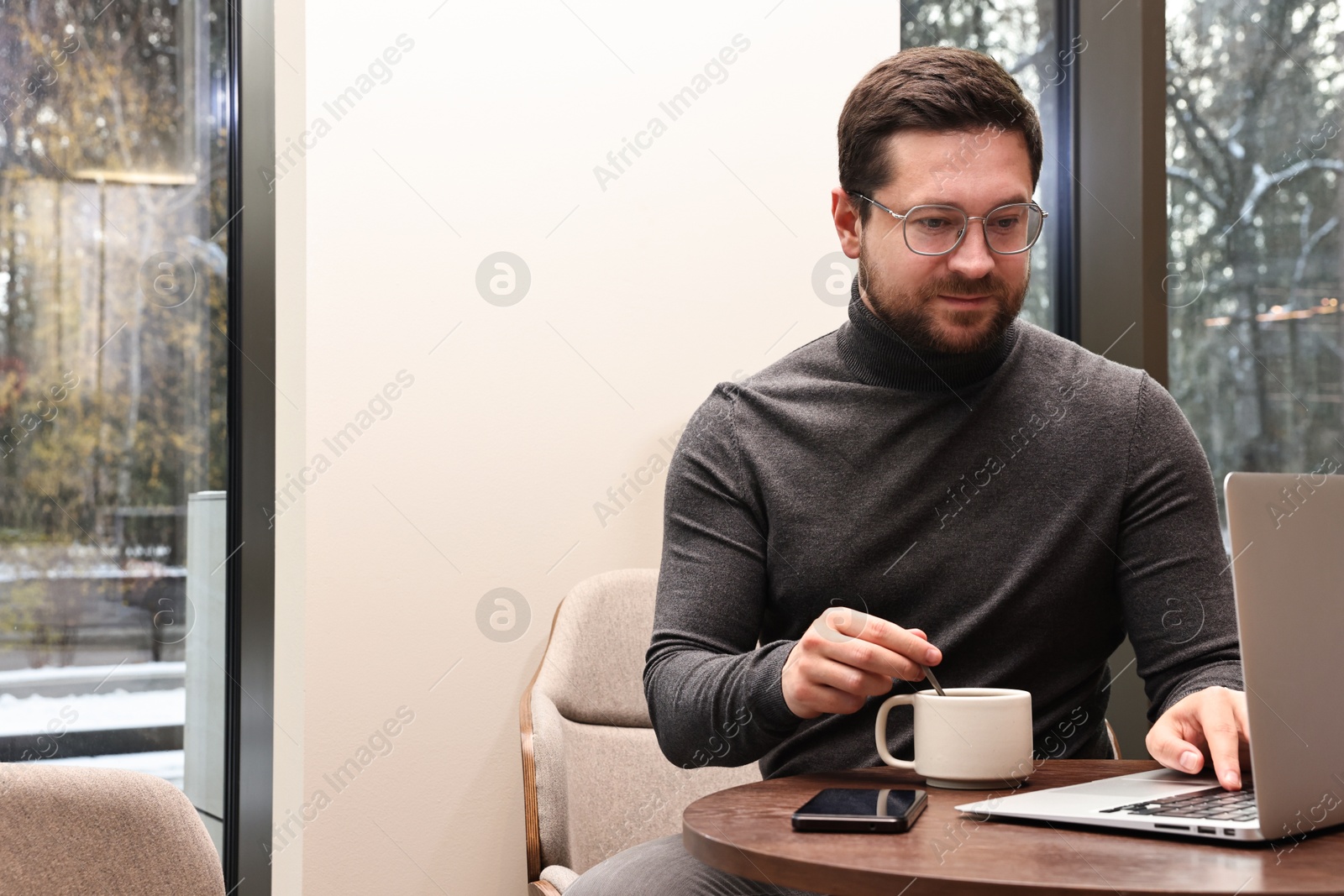 Photo of Businessman with laptop having coffee break at wooden table in cafe. Space for text