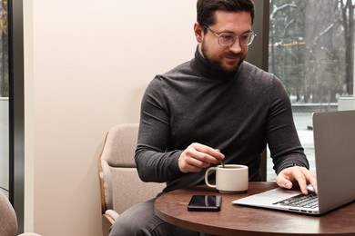 Photo of Businessman with laptop having coffee break at wooden table in cafe. Space for text