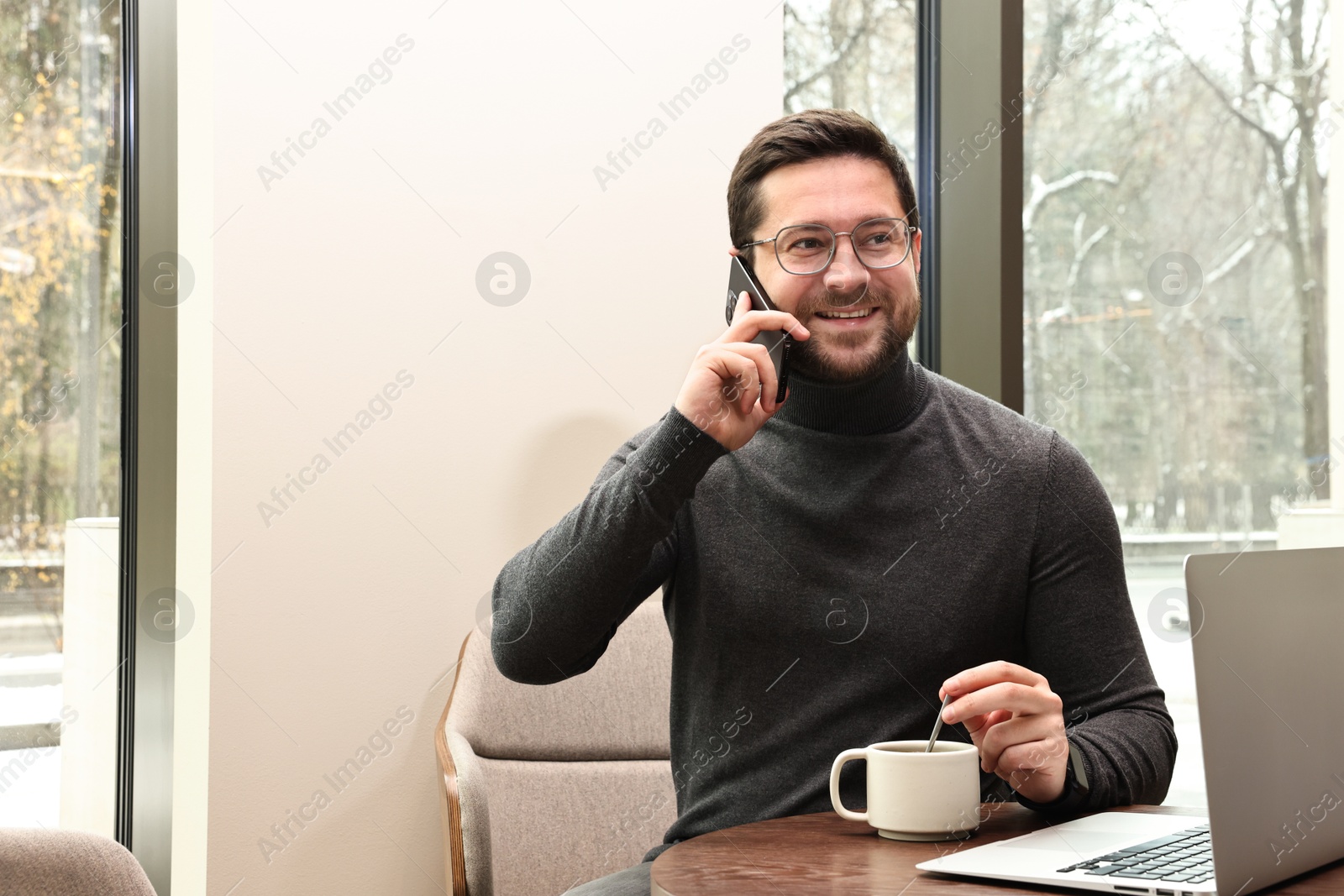 Photo of Smiling businessman talking on smartphone during coffee break in cafe. Space for text