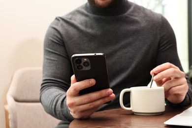 Photo of Man with smartphone having coffee break at wooden table in cafe, closeup