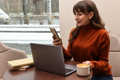 Photo of Smiling woman with smartphone having coffee break at wooden table in cafe