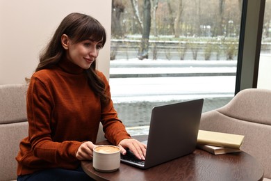 Photo of Beautiful woman with laptop having coffee break at wooden table in cafe