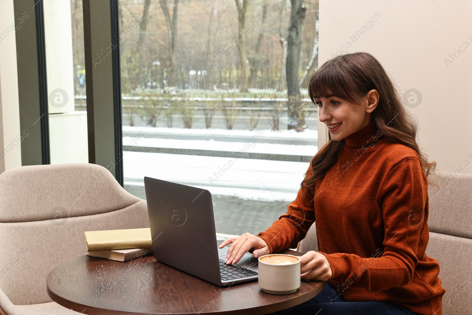 Photo of Smiling woman with laptop having coffee break at wooden table in cafe