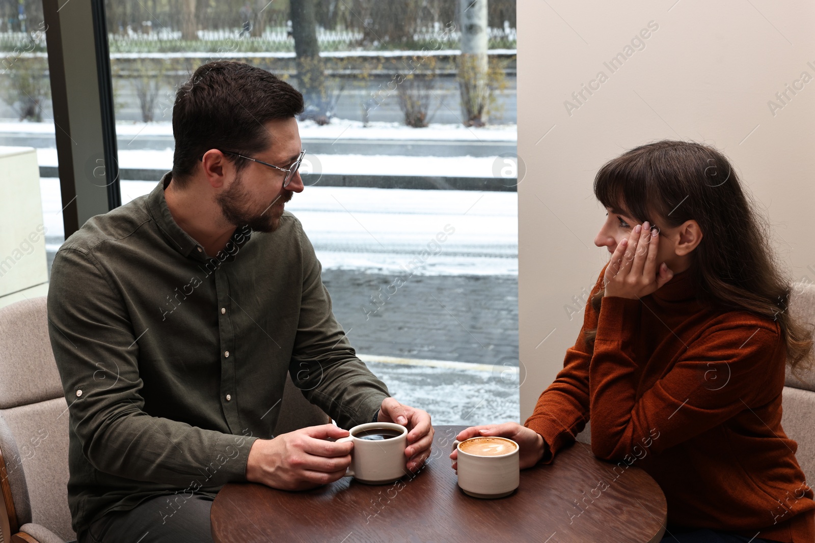 Photo of Colleagues talking during coffee break at wooden table in cafe