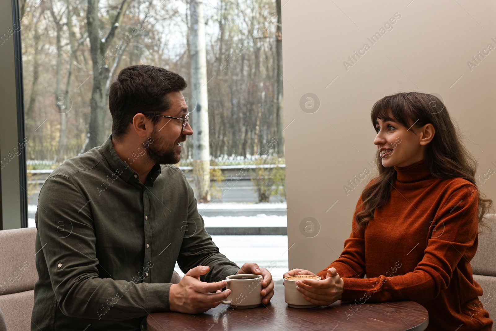 Photo of Happy colleagues talking during coffee break at wooden table in cafe