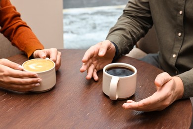 Photo of Colleagues having coffee break at wooden table in cafe, closeup