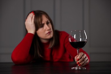 Alcohol addiction. Woman with glass of red wine at wooden table indoors, selective focus