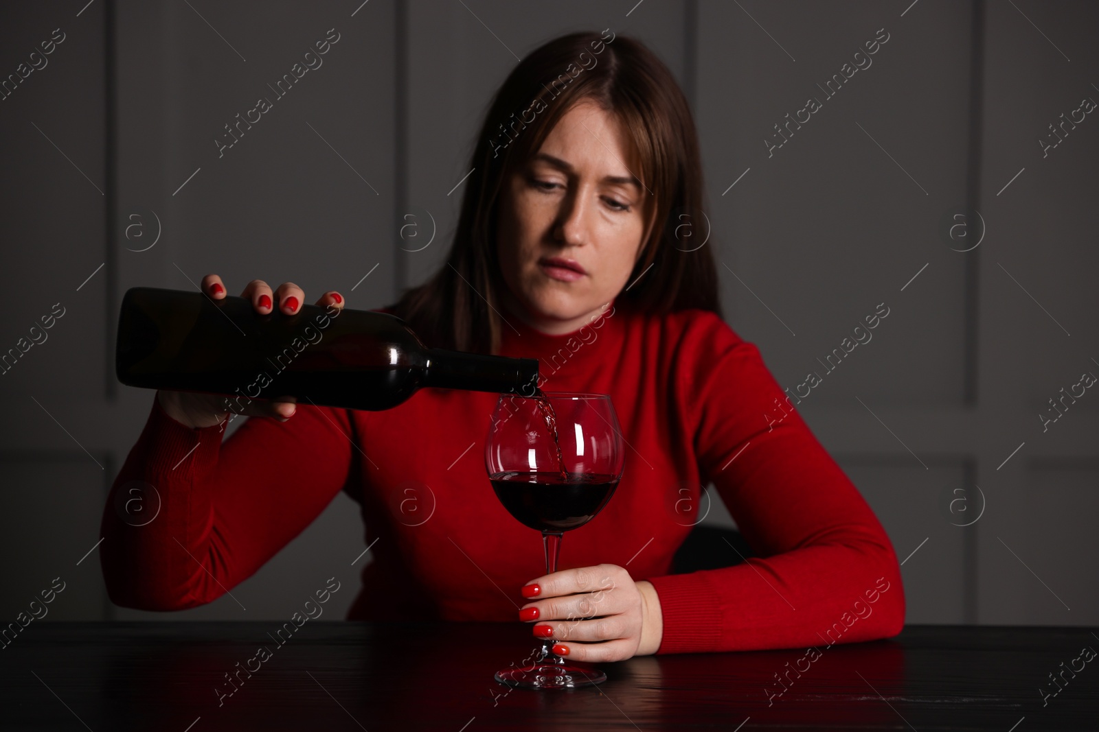 Photo of Alcohol addiction. Woman pouring red wine into glass at wooden table indoors