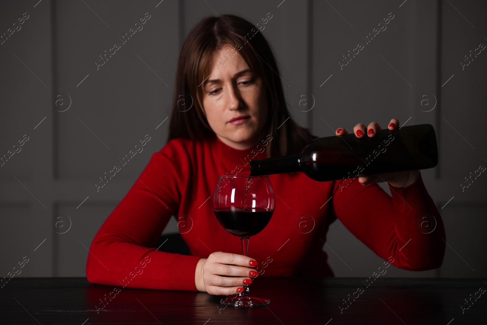 Photo of Alcohol addiction. Woman pouring red wine into glass at wooden table indoors