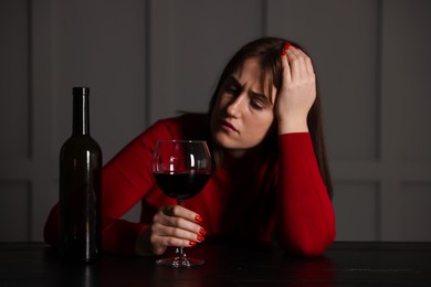 Photo of Alcohol addiction. Woman with glass of red wine and bottle at wooden table indoors