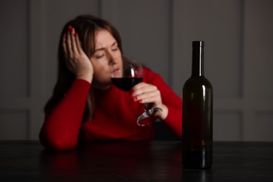 Photo of Alcohol addiction. Woman drinking red wine at table indoors, focus on bottle