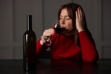 Alcohol addiction. Woman drinking red wine at table indoors, focus on bottle