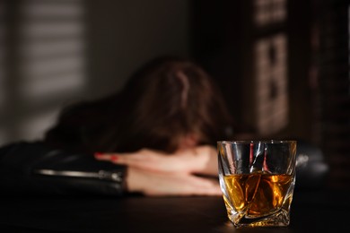 Photo of Alcohol addiction. Woman at table indoors, focus on glass of whiskey