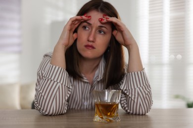 Photo of Alcohol addiction. Woman at wooden table with glass of whiskey indoors, selective focus