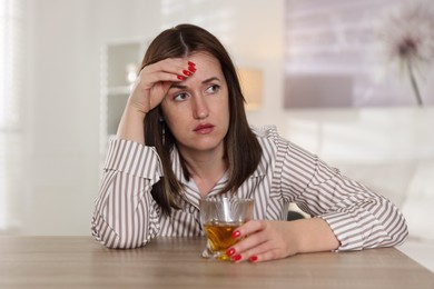 Photo of Alcohol addiction. Woman with glass of whiskey at wooden table indoors