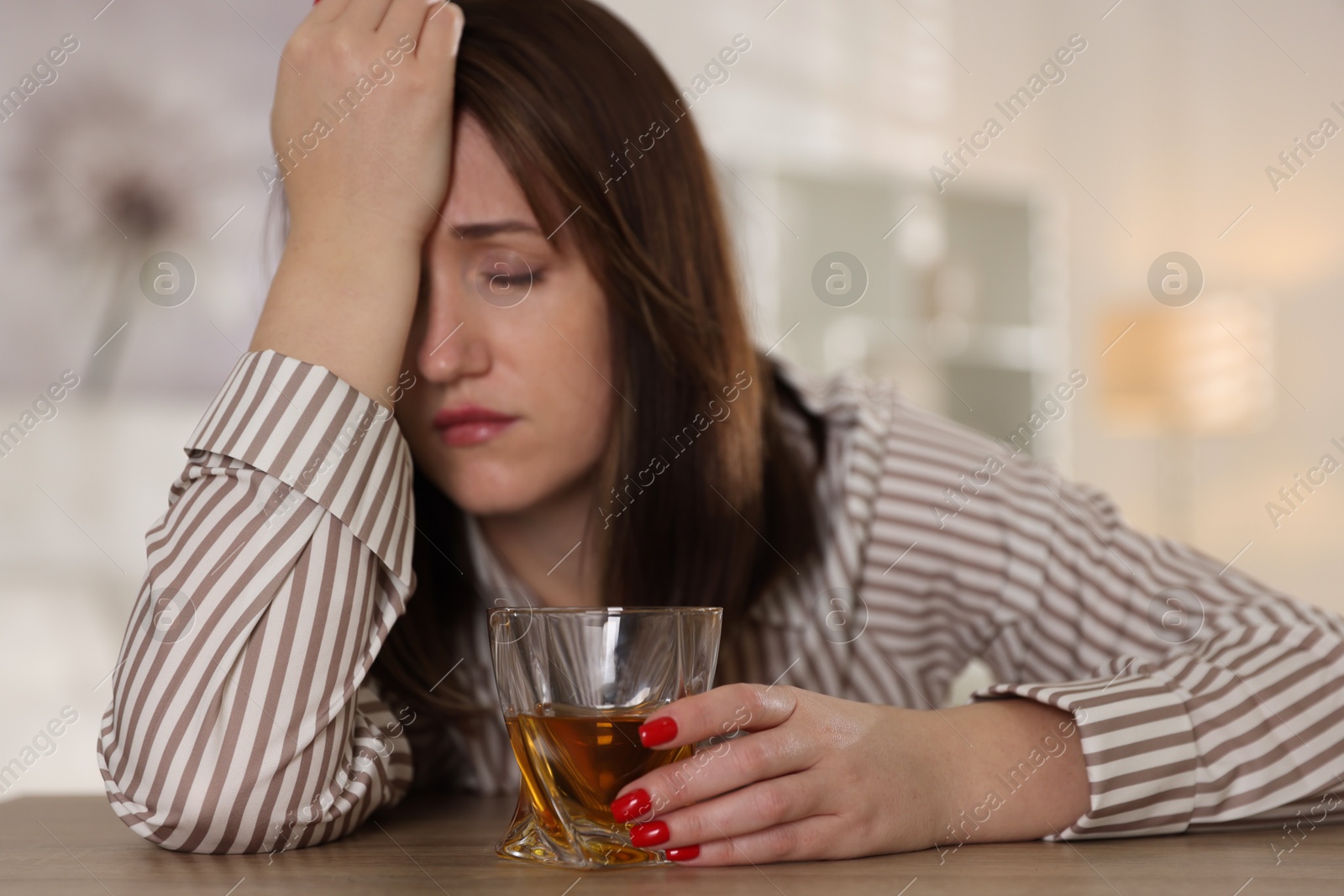 Photo of Alcohol addiction. Woman with glass of whiskey at wooden table indoors, selective focus