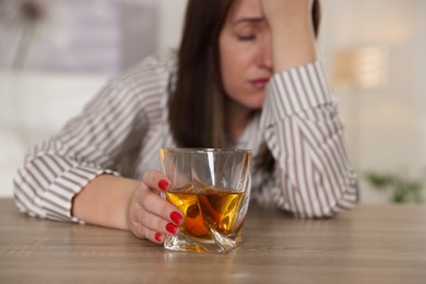 Photo of Alcohol addiction. Woman with glass of whiskey at wooden table indoors, selective focus