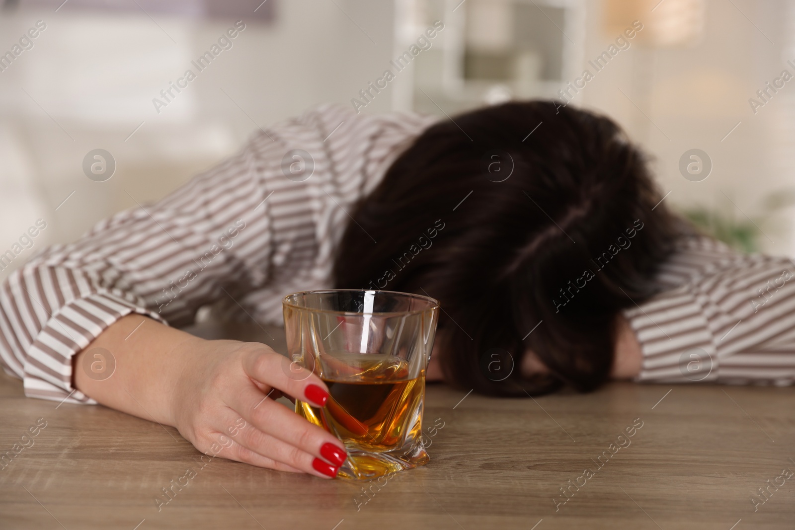 Photo of Alcohol addiction. Woman with glass of whiskey at wooden table indoors, selective focus