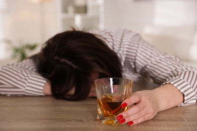 Photo of Alcohol addiction. Woman with glass of whiskey at wooden table indoors, selective focus