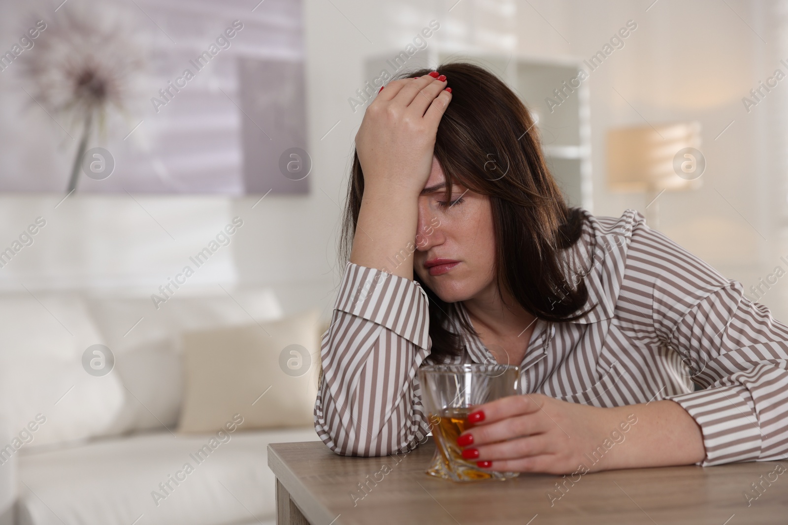 Photo of Alcohol addiction. Woman with glass of whiskey at wooden table indoors, space for text