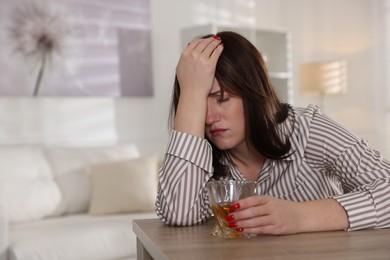 Photo of Alcohol addiction. Woman with glass of whiskey at wooden table indoors, space for text